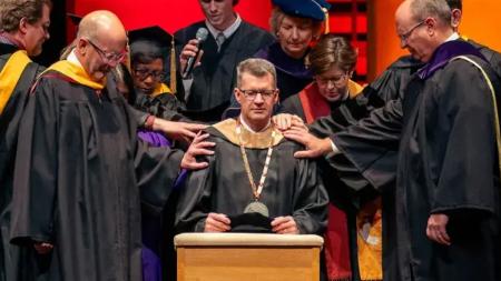 Student body president Tyler VerMerris joins with ceremony participants in the laying on of hands and in offering a prayer for Calvin’s new president, Greg Elzinga.