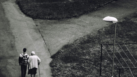 a teenager walks and elderly woman down the street