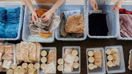 An overhead shot of a table that has containers with cans of soup, crackers, and clothing donations