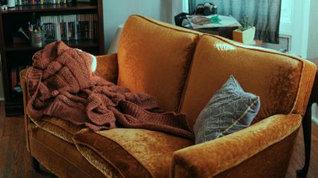 A cozy couch with a blanket and a pillow