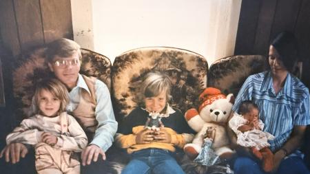 A family of five sitting on a couch. There is a mom, dad, and two children, and a baby