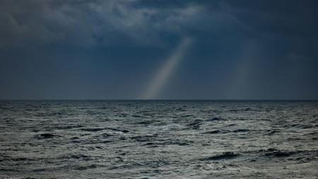 Dark sky with a light streak over the ocean