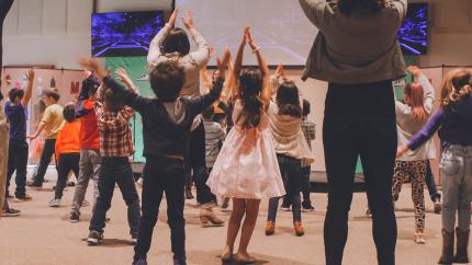 young kids raise their hands in the air in a multi-purpose room