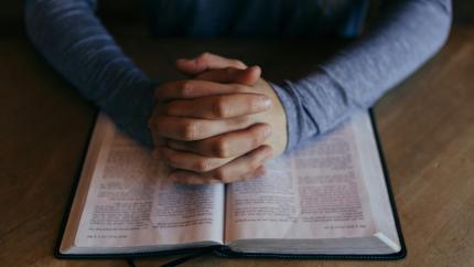 Hands folded in prayer on open Bible