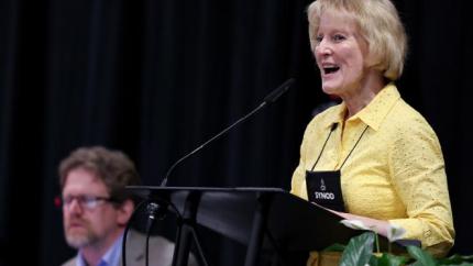 Shirley Roels speaks into a microphone at Synod 2025