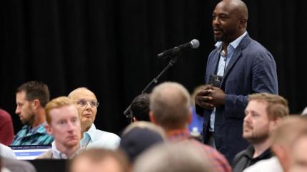 Chris Samuels speaks in a microphone at Synod