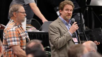 Zach King speaking into a microphone at Synod