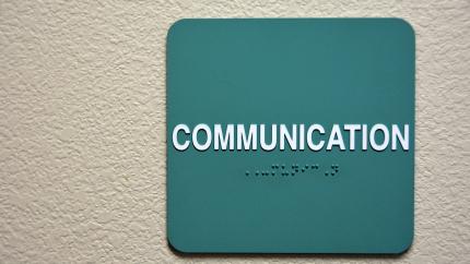 A wall sign that says Communication with braille underneath