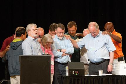 Synod delegates pray for Bob DeMoor and The Banner staff.