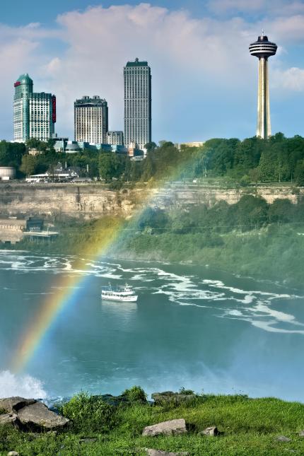 A rainbow over Niagara Falls with a boat and skyline in back