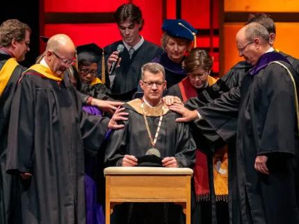 Student body president Tyler VerMerris joins with ceremony participants in the laying on of hands and in offering a prayer for Calvin’s new president, Greg Elzinga.