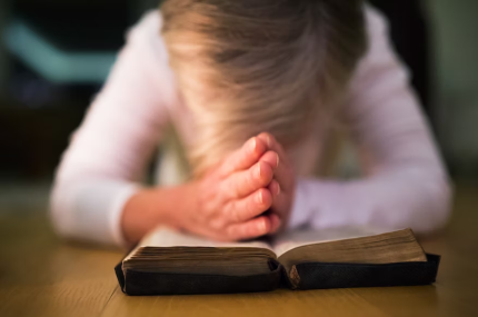 a head bowed in prayer over and open Bible