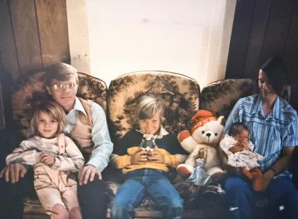 A family of five sitting on a couch. There is a mom, dad, and two children, and a baby