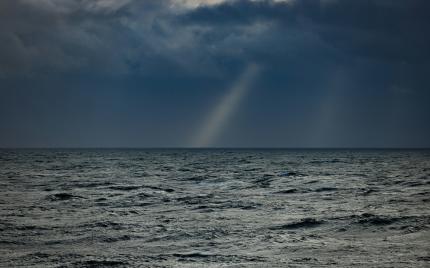 Dark sky with a light streak over the ocean