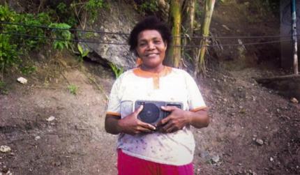 Bertha happily holds a radio on which she listens to BTGMI programs.