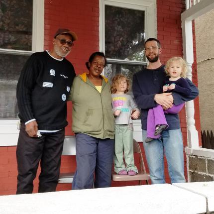 Pastor Nate Morris, Sis, and Kurt Riexinger and his daughters, Abigail and Emmaline, stand on porch of Germantown Peace Church .
