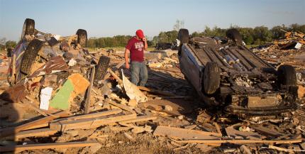 A man talks on his phone as he looks for his cat near an upturned in a suburban area following a tornado near Vilonia, Arkansas.
